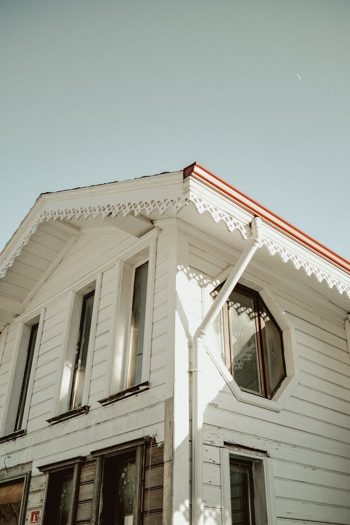A charming white wooden house with decorative trim and red roof under a clear sky.