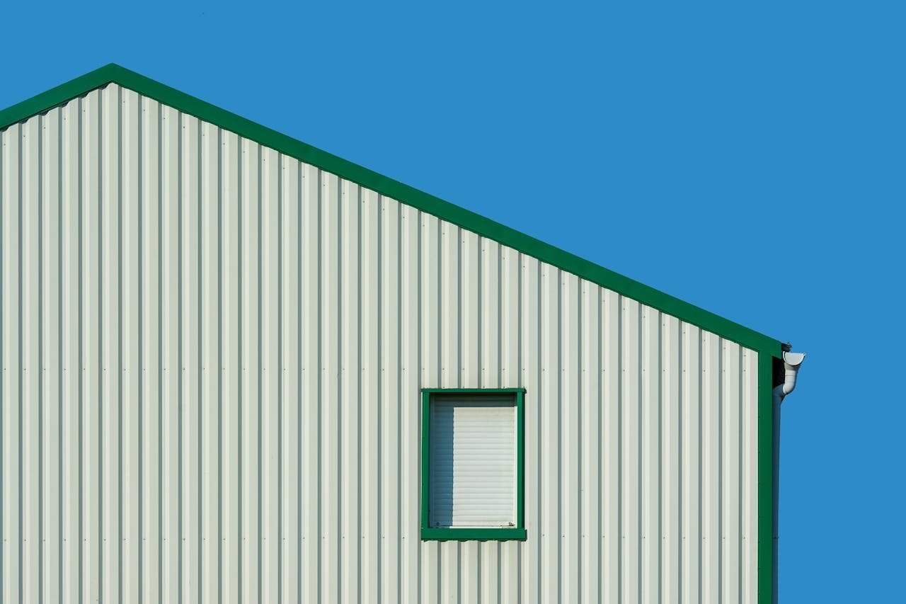 Minimalist building facade against bright blue sky, featuring vertical panels and a single window.